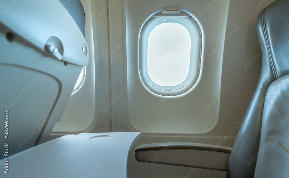 Plane window with white sunlight. Empty plastic airplane tray table at seat back. Economy class airp