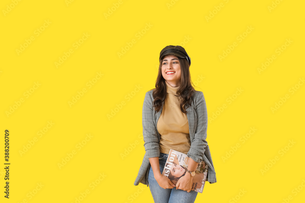 Stylish young woman in autumn clothes and with fashion magazine on color background