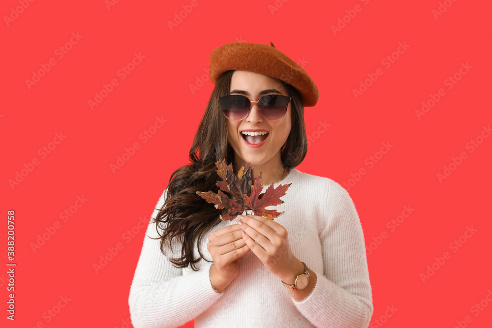 Happy young woman with autumn leaves on color background