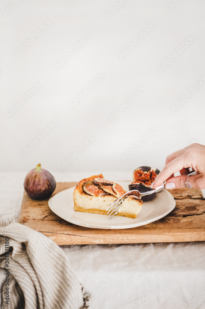 Hand of woman eating homemade gluten free fig cheesecake with fresh figs on white plate over rustic 