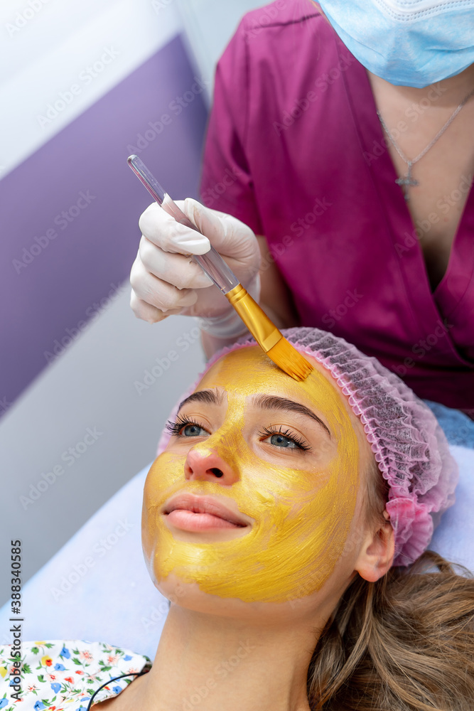一位年轻女子，闭着眼睛，脸上戴着金色口罩，躺在美容诊所的沙发上，做水疗手术。