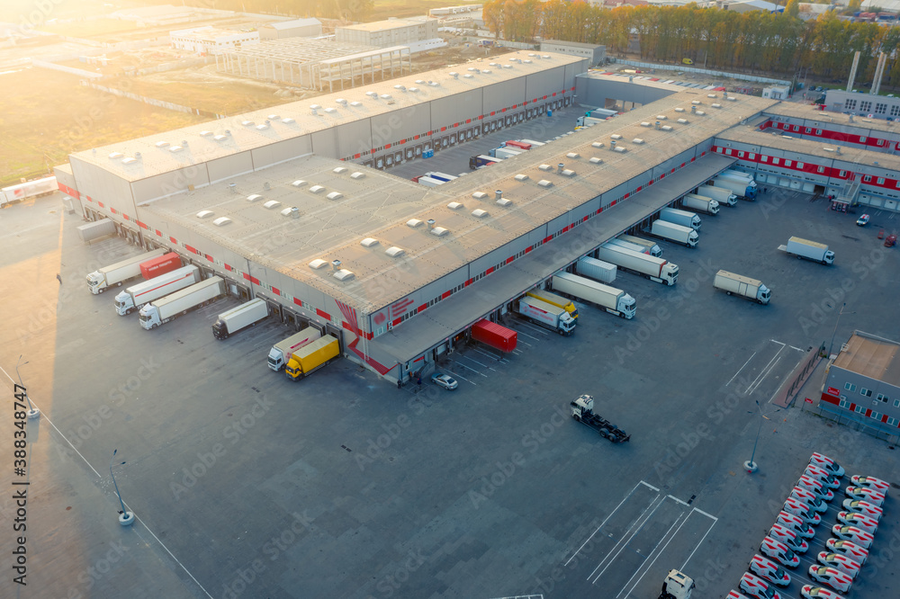 Logistics park with warehouse, loading hub and many semi trucks with cargo trailers standing at the 