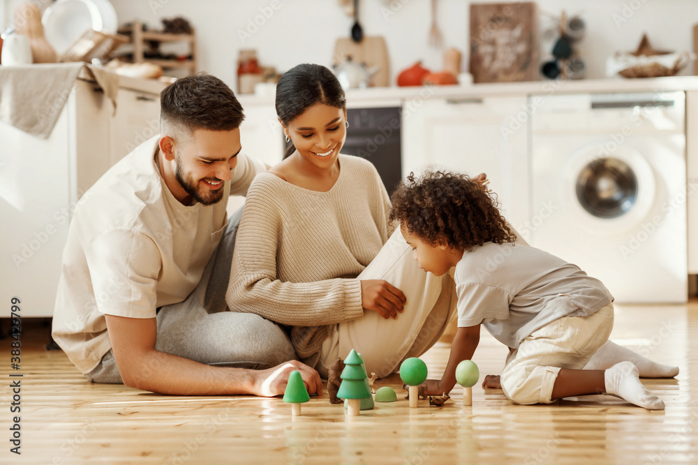 Diverse parents playing with son in kitchen.