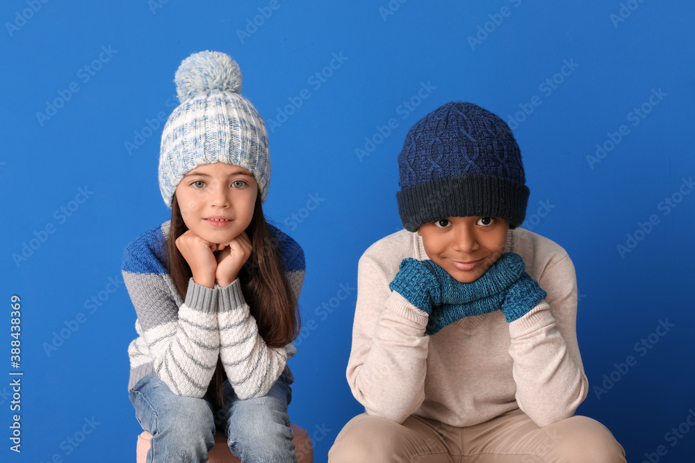 Cute children in winter clothes on color background