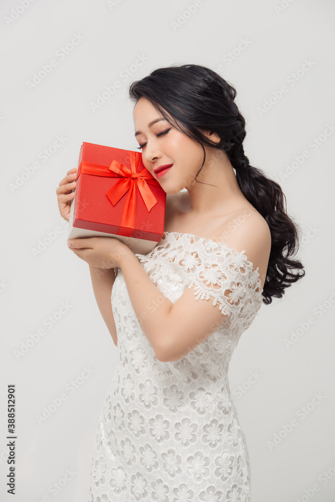 快乐的年轻优雅的亚洲女人，拿着特别的礼盒，穿着白底连衣裙。