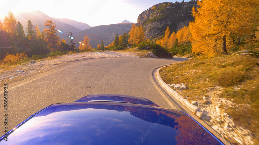 CLOSE UP: Blue car cruises along an empty scenic road in the Dolomites at sunset