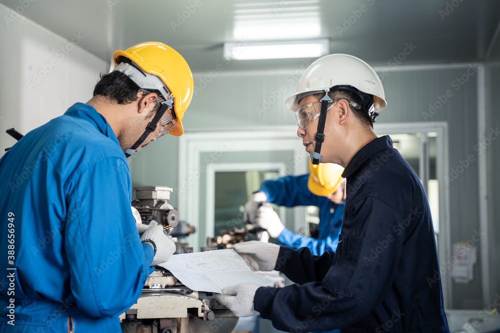 一名亚洲工程师正在培训他的工人进行重型机械加工。
