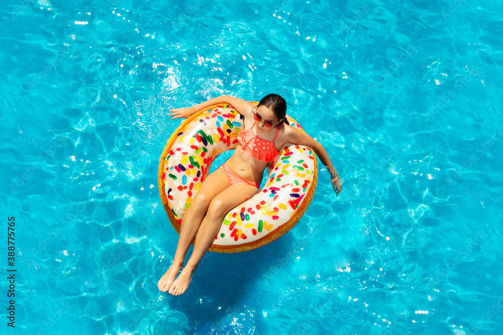 Curly teenage girl in sunglasses in water swim on inflatable ring doughnut view from above
