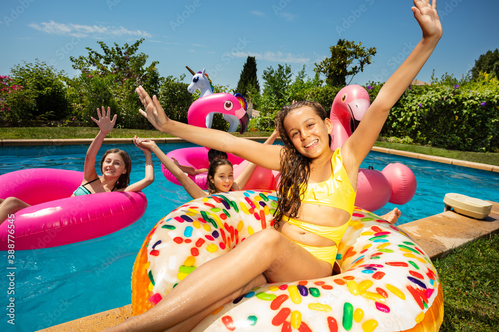 Smiling girl in group of friends play, have fun in swimming pool outside pose with inflatable doughn