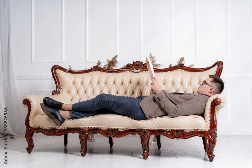 Young businessman rests on on stylish sofa. Man reading magazine while laying on settee.