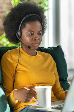 Afro-American consultant woman wear headphones remote work on computer during lockdown, drinking tea