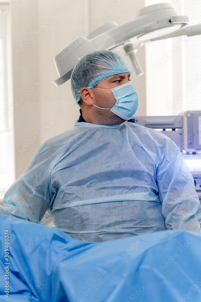 医生戴着口罩、磨砂膏和乳胶手套。外科医生在明亮的现代外科手术中进行手术
