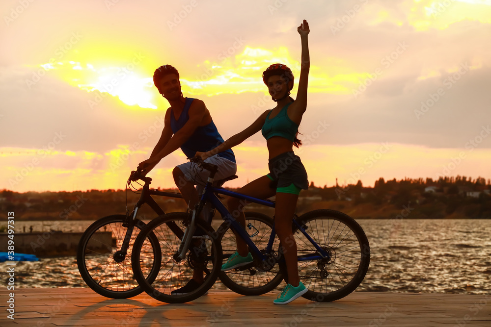 Sporty young cyclists riding bicycles near river at sunset