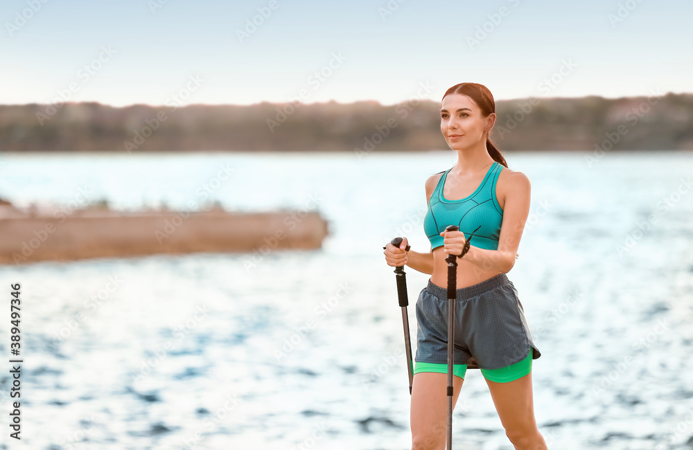 Young woman training with walking poles near river
