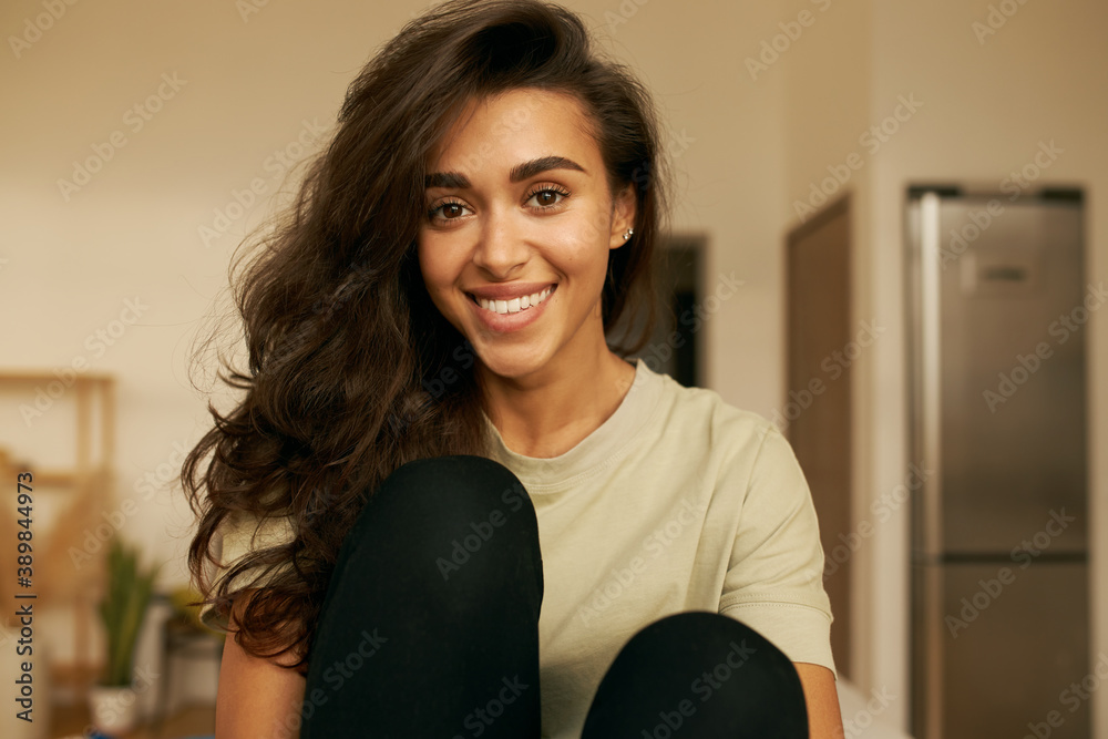 Indoor shot of beautiful happy young 20 year old Arabic woman relaxing at home wearing comfy clothin