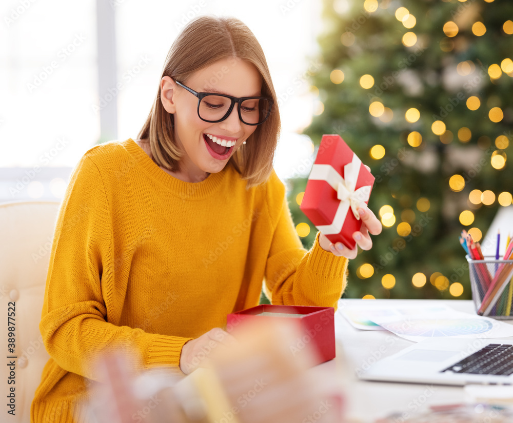 快乐女孩自由职业者在圣诞节前在家庭办公室打开一份节日礼物。
