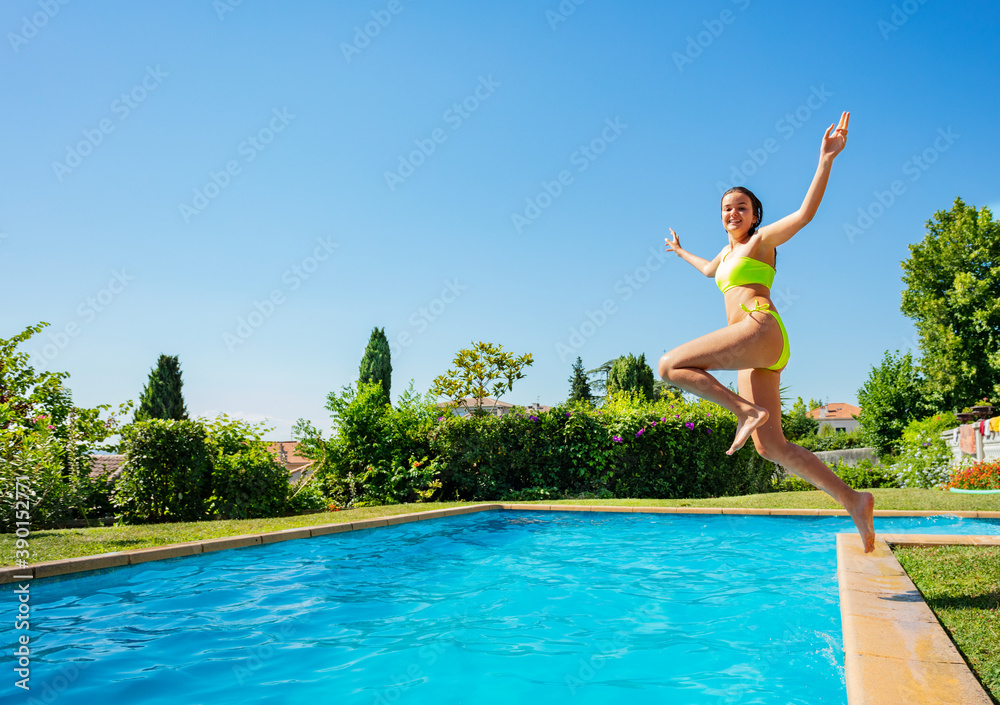 Teenage girl jump in mid air into the swimming pool view from side scream and smile with hands up in