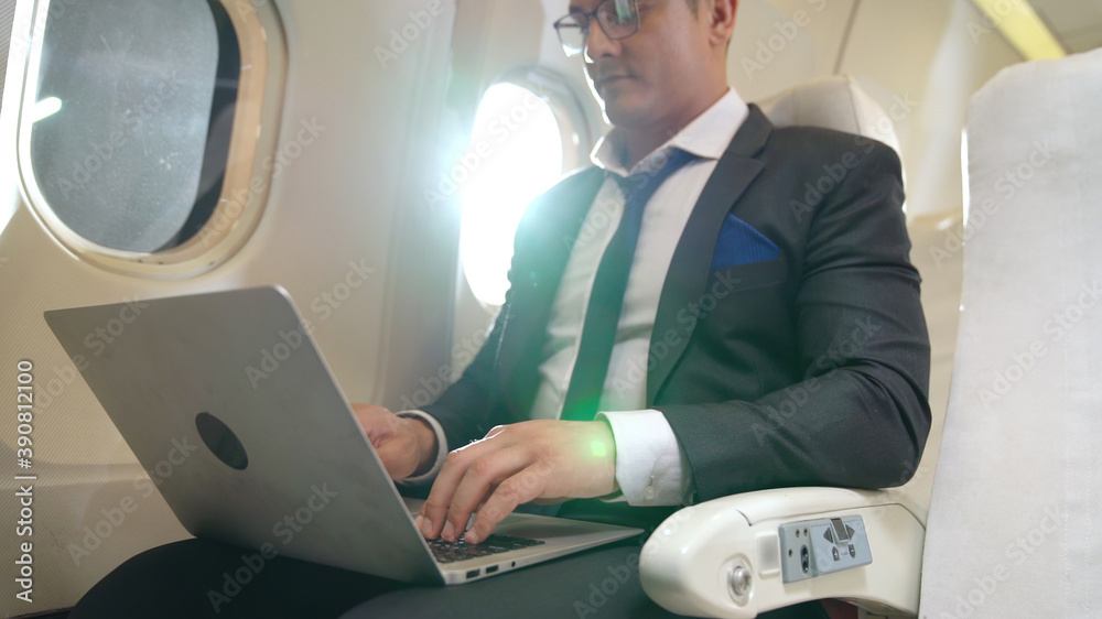 年轻的商人在飞机上使用笔记本电脑。商务旅行的概念。