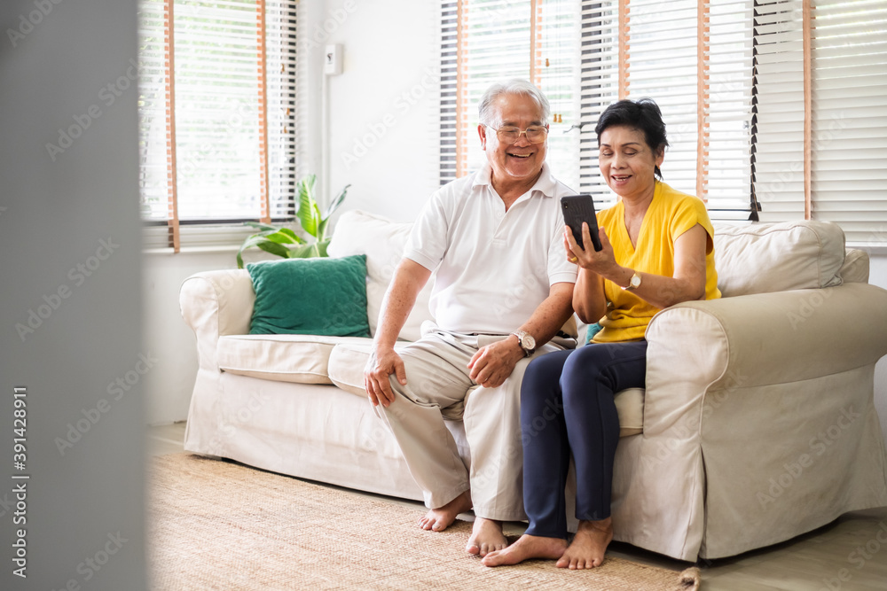 亚洲老年夫妇（白发）在家客厅的沙发上用手机放松，老年人与