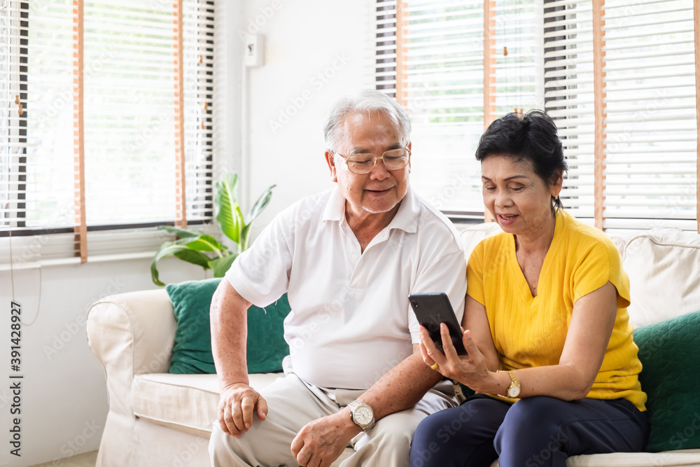 亚洲老年夫妇（灰色头发）使用手机在家客厅的沙发上放松，老年人与