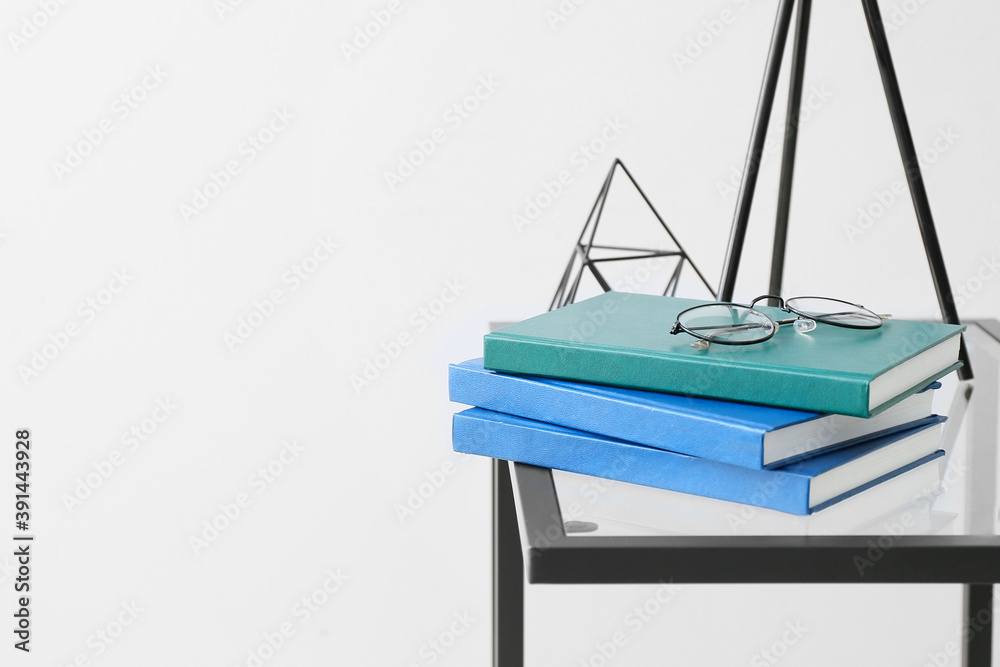 在浅色背景下，桌子上放着一摞书和眼镜