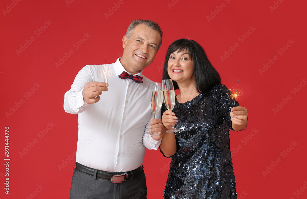Mature couple with Christmas sparklers and champagne on color background