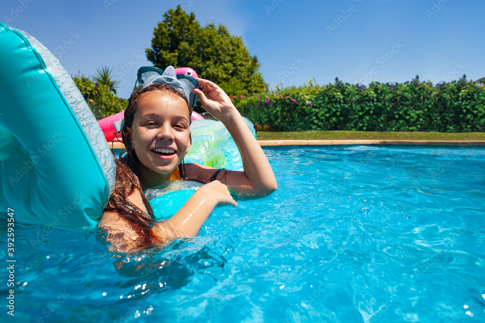 Happy little girl with scuba mask swim on matrass in swimming pool outside