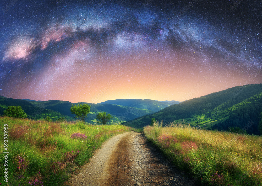 Arched Milky Way over the mountain dirt road in summer. Beautiful night landscape with starry sky, m