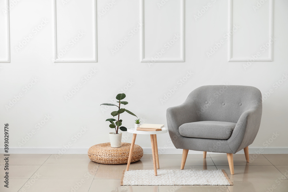 时尚的扶手椅，配有桌子、书籍和室内植物，靠近室内的浅色墙壁