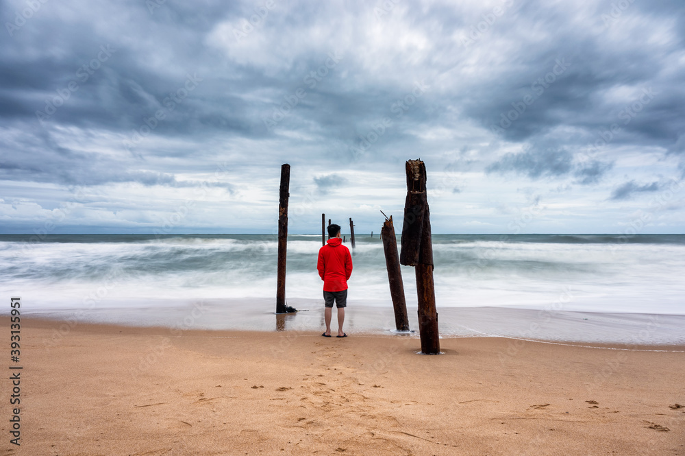 皮莱海滩暴风雨天气下，一名男子站在海滩上，大浪袭击了腐烂的木桥