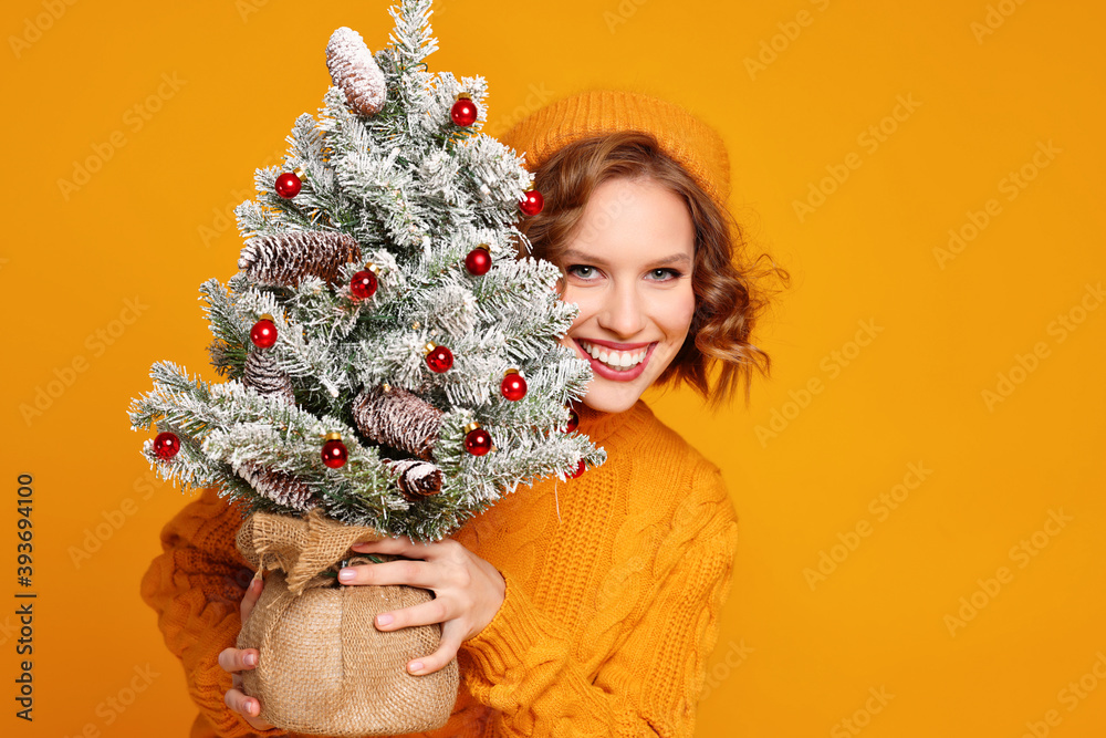 快乐的女人微笑着，手里拿着一棵黄色背景的小圣诞树。