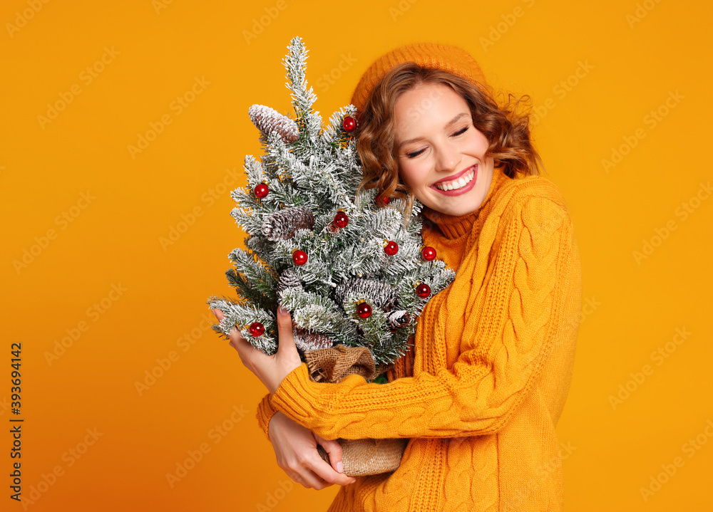 快乐的女人微笑着，手里拿着一棵黄色背景的小圣诞树。