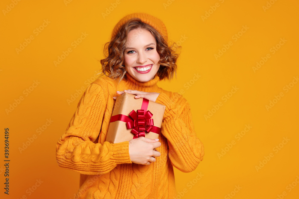 快乐的女人微笑着，拿着一份黄色背景的圣诞礼物。