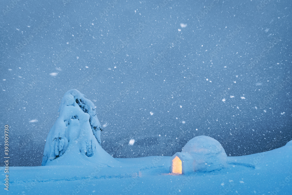 冬季山脉草地上的雪冰屋从内部发光。晚上雪覆盖着冷杉