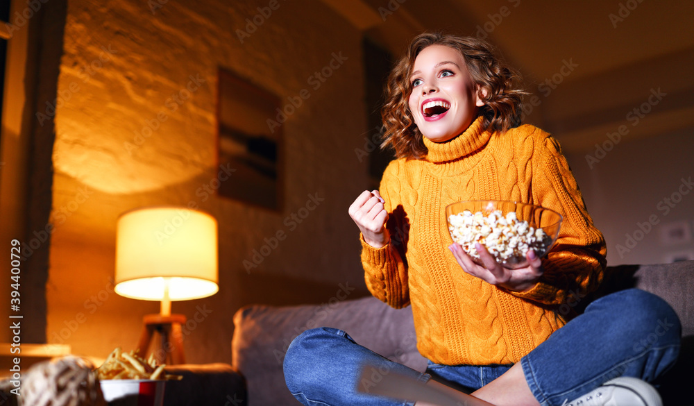 年轻快乐的女人拿着爆米花，晚上在家里笑着看电视电影