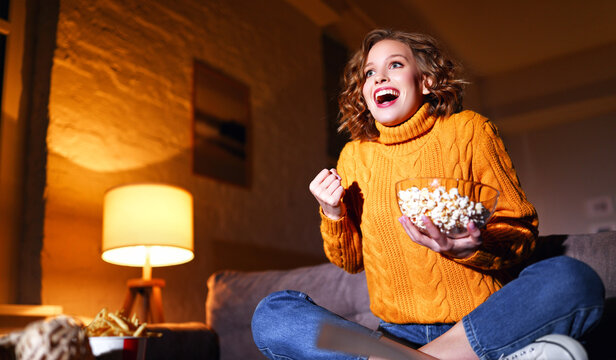 年轻快乐的女人拿着爆米花，晚上在家里笑着看电视电影