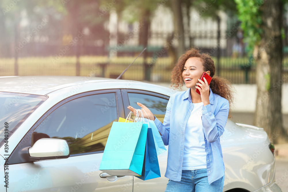 非裔美国妇女拿着购物袋在户外汽车附近打电话