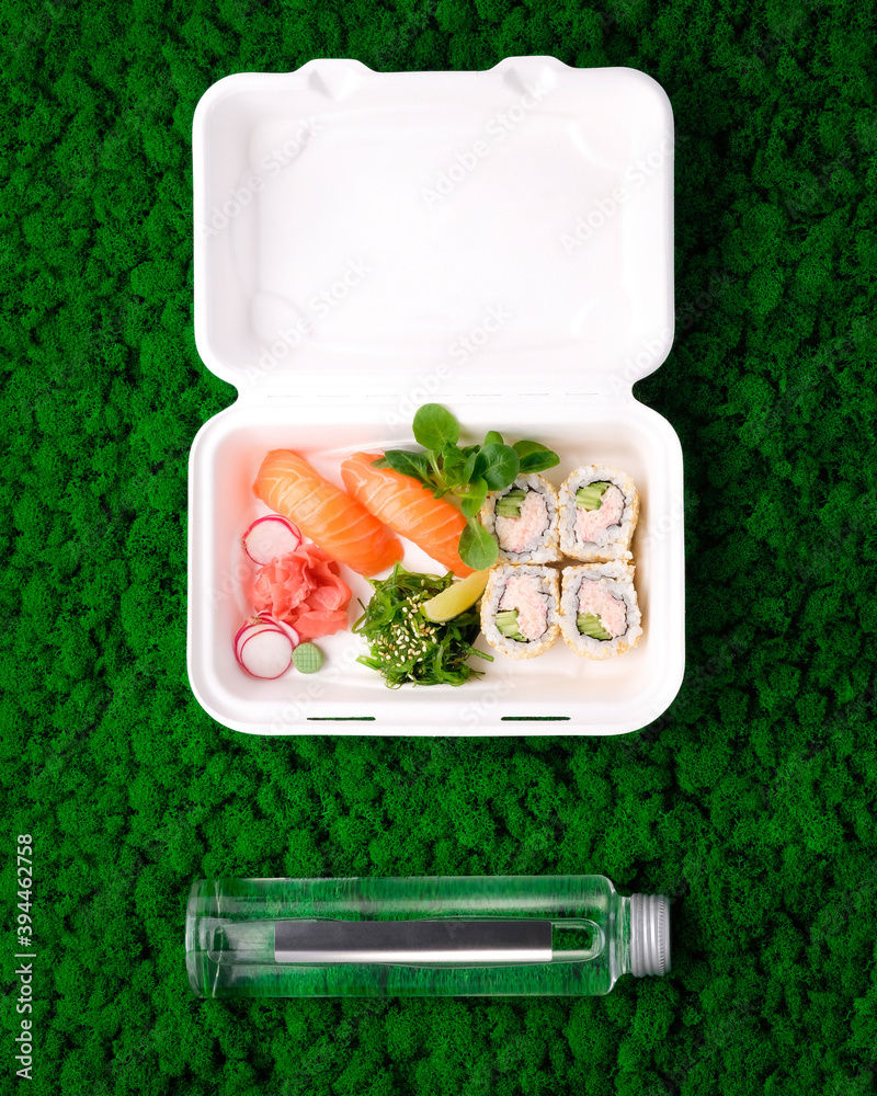 寿司装在外卖盒里，玻璃瓶里的水放在绿苔背景上。三文鱼生鱼片，Califo
