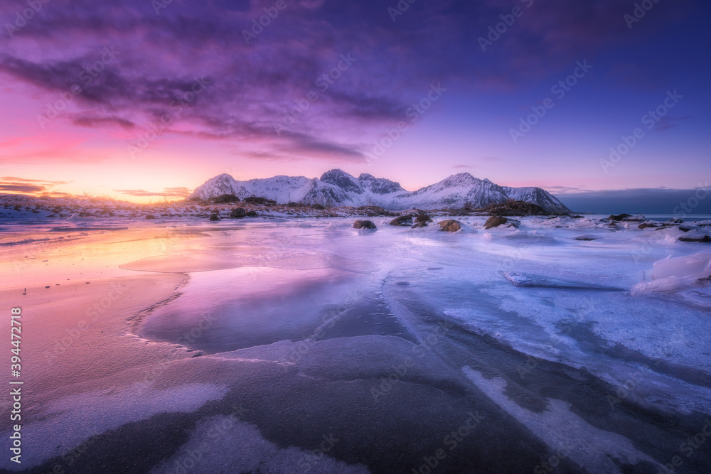 Frozen sea coast at colorful sunset in Lofoten islands, Norway. Snowy mountains, sea with frosty sho