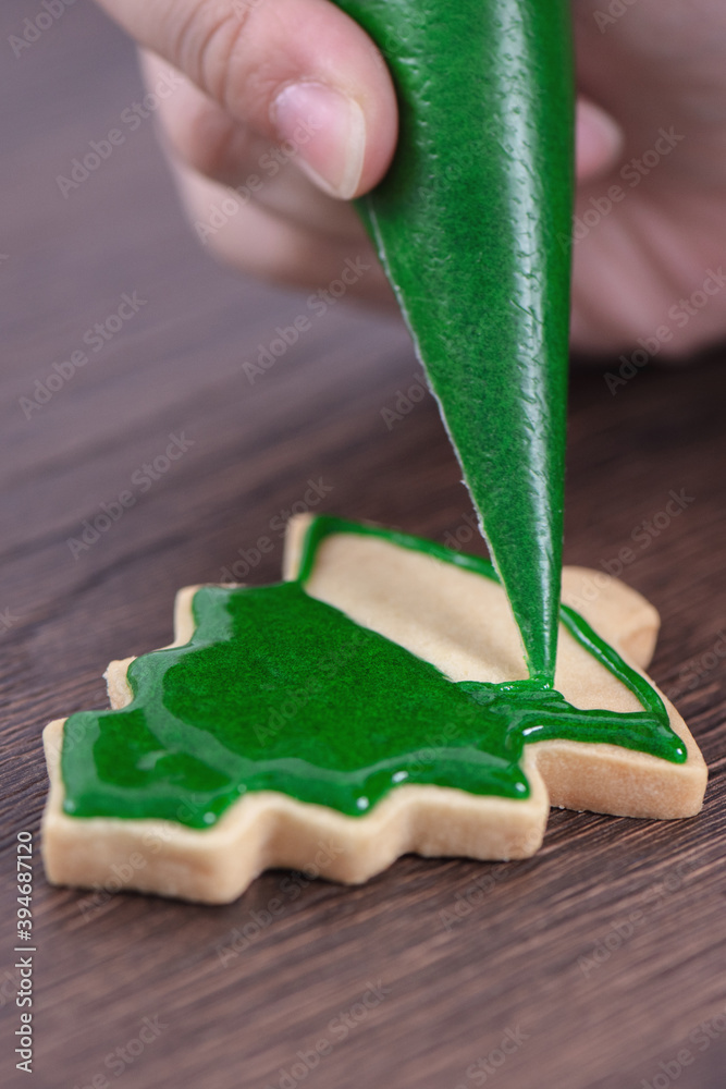 用糖霜在木桌背景上绘制圣诞树糖饼的特写。