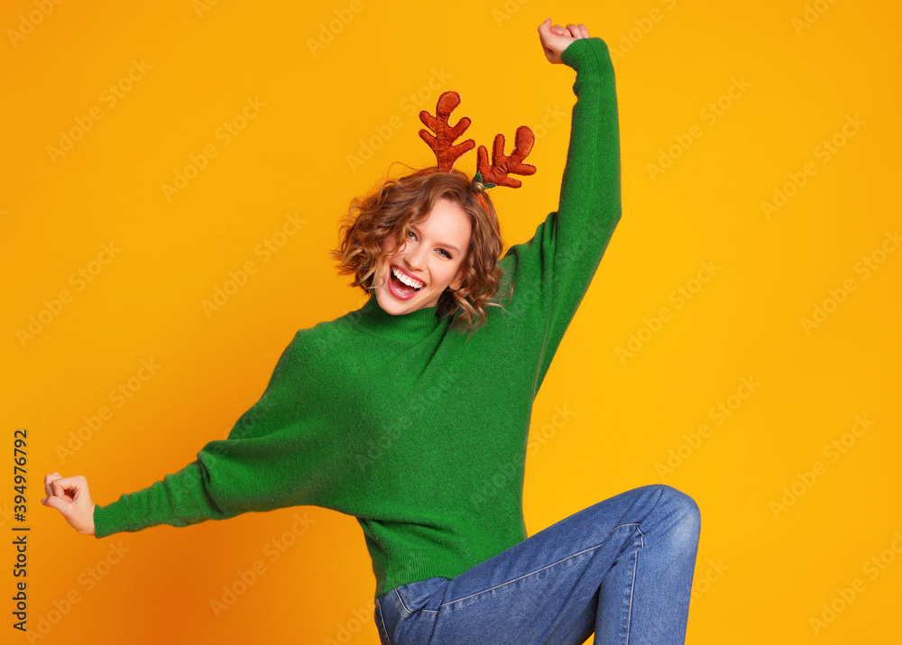 带着圣诞鹿角的快乐快乐的女人跳舞，享受着黄色背景的生活