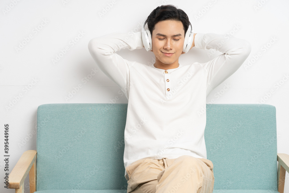 亚洲商人坐在家里的沙发上戴着无线耳机听音乐