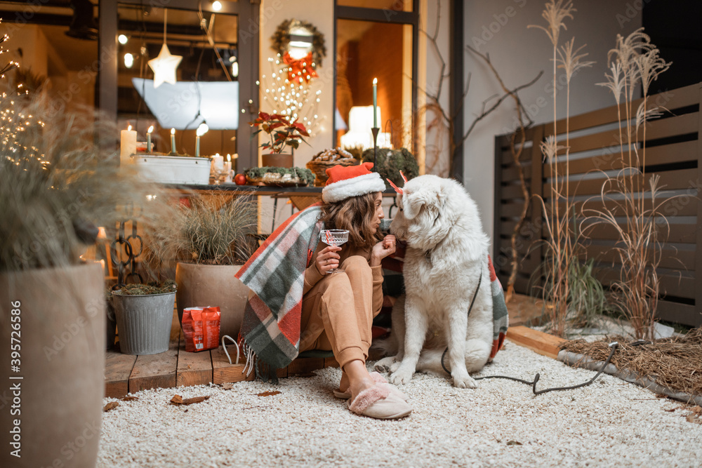 戴着圣诞帽的女人和她的可爱的狗一起庆祝新年假期，坐在床上