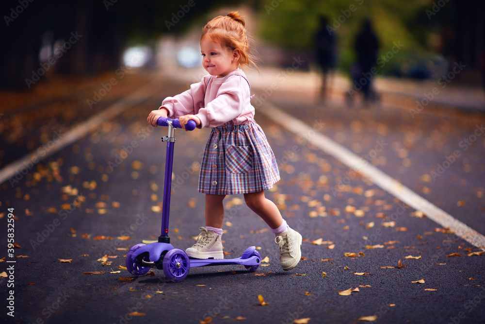 可爱的红头发小女孩在秋季公园滑板车