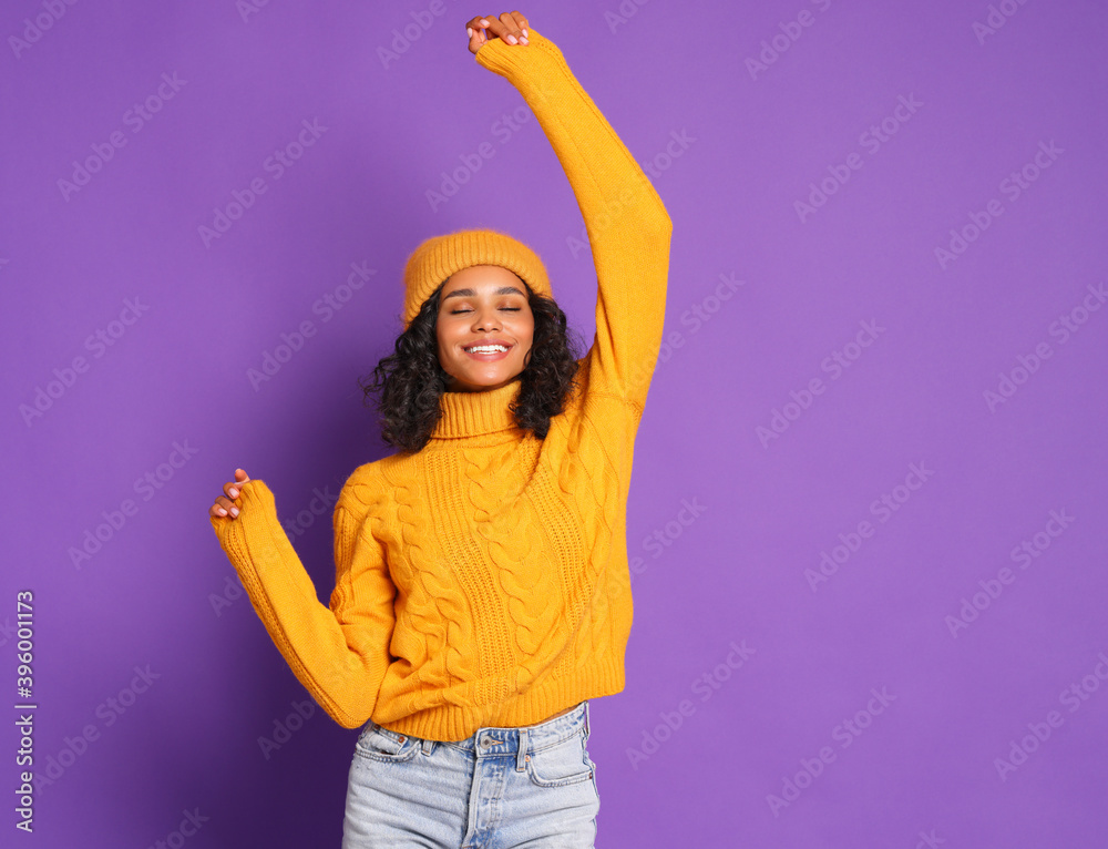 穿着黄色毛衣、戴着帽子的开朗的非裔美国妇女跳舞，享受多姿多彩的生活