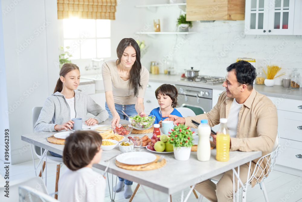 分享食物。一位体贴的西班牙妇女站在厨房里为丈夫和孩子端上沙拉