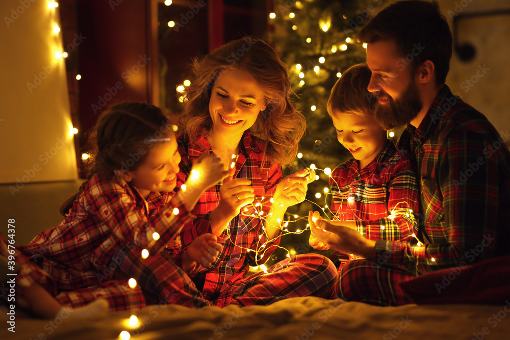 圣诞快乐！家里树旁的床上戴着发光的花环，幸福的一家人