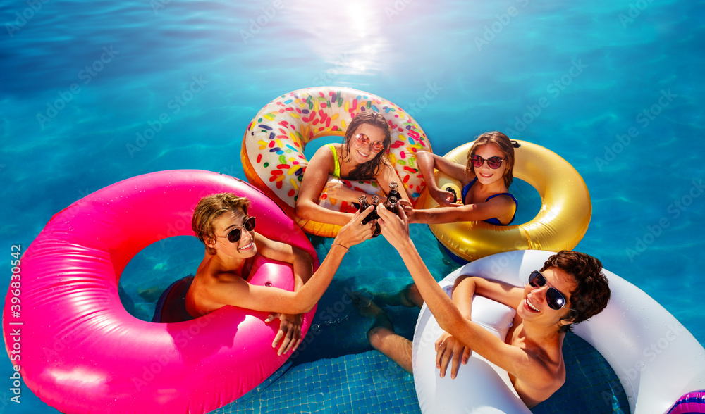 一群青少年在游泳池里用充气玩具甜甜圈从上面喝苏打水