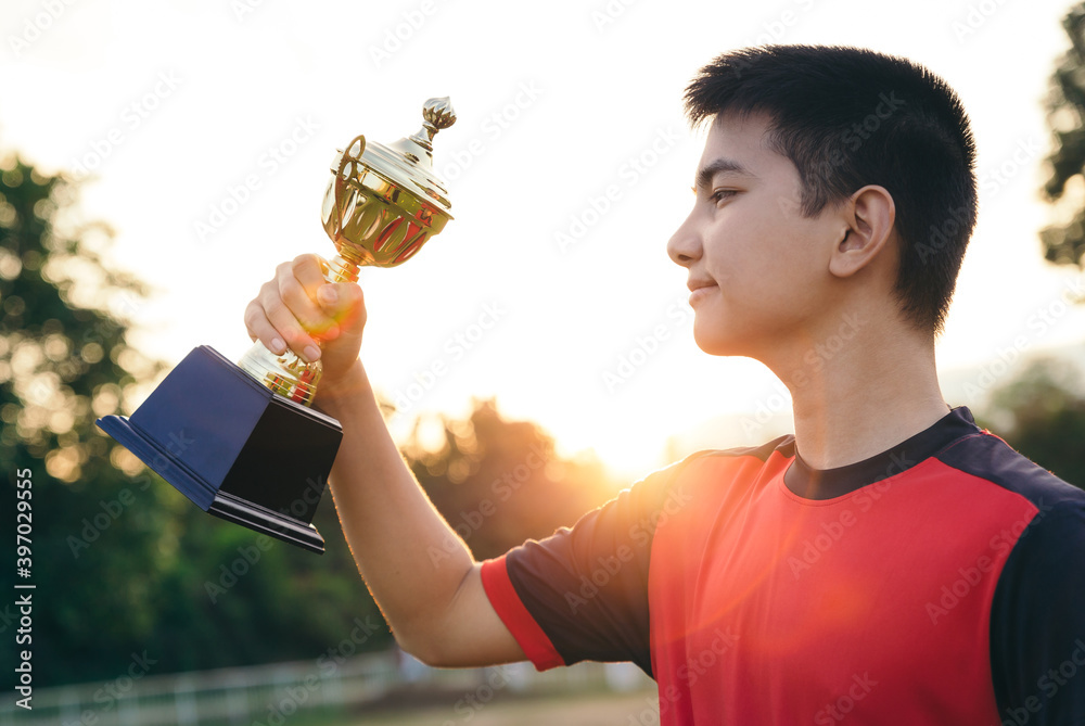 亚洲青少年足球运动员手持奖杯，摆出庆祝姿势。