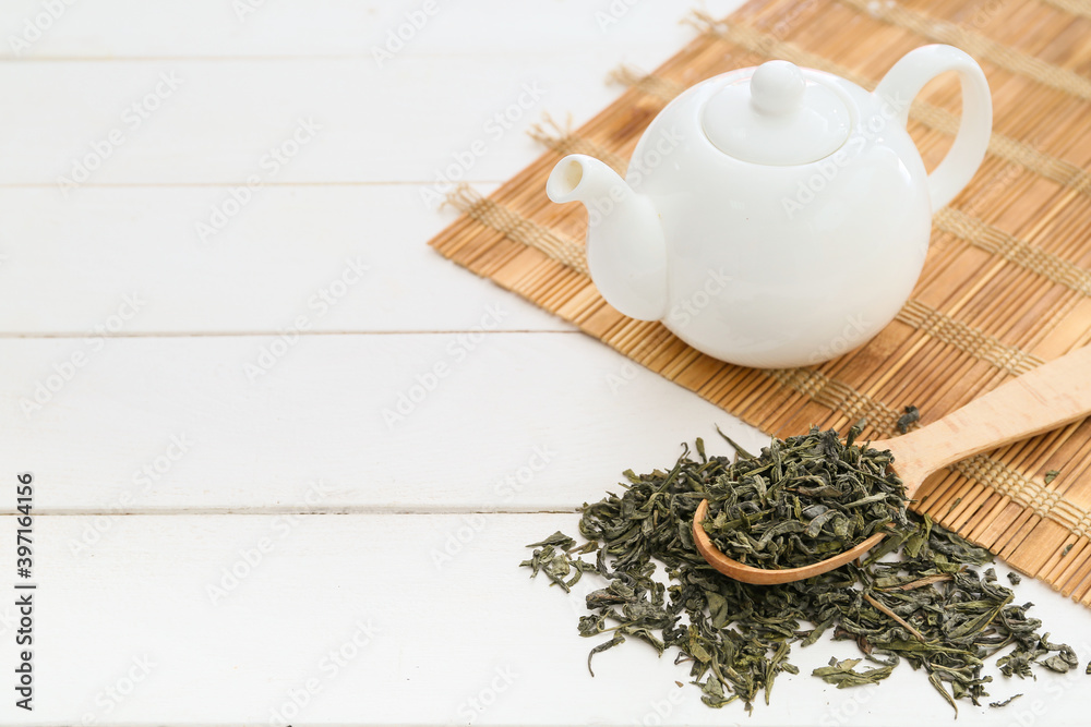 盛有干绿茶和茶壶的勺子放在浅色桌子上